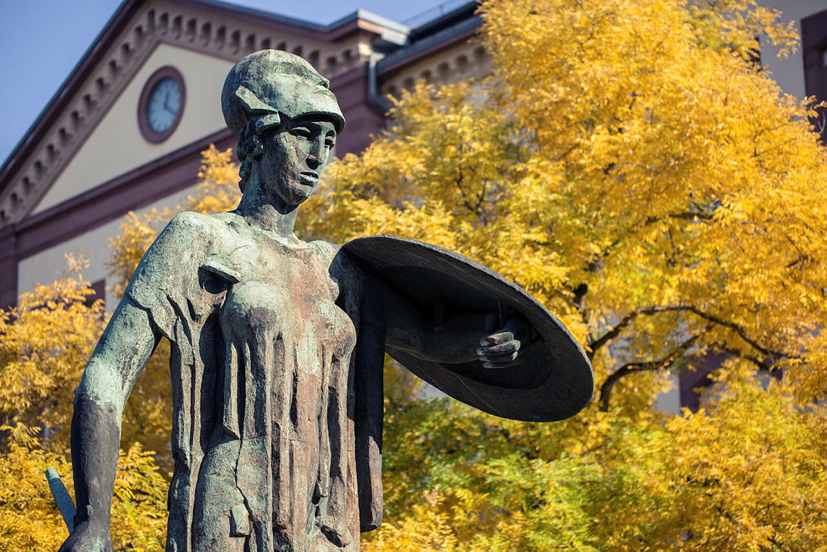 Bronze statue of a person with billiard cue at a historic building